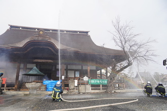 曼陀羅寺正堂に向けて放水訓練を行う消防署と消防団第4分団の写真